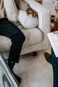 From above crop African American male in casual clothes sitting on comfy couch and answering professional female consultant questions in modern psychotherapy office