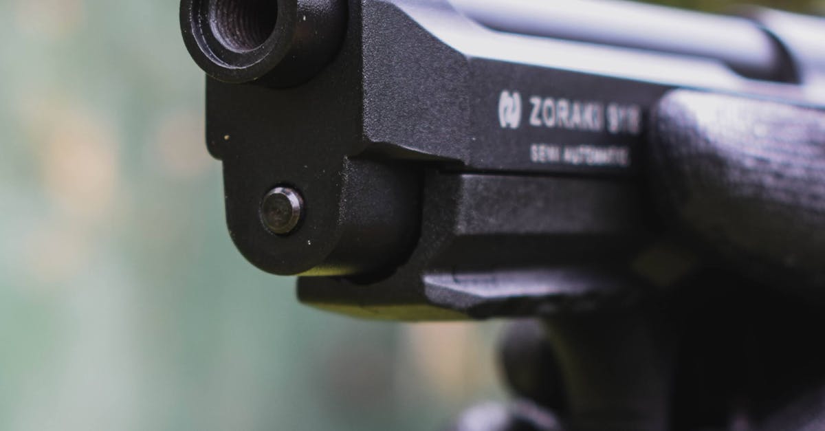 A detailed close-up of a gloved hand holding and aiming a semi-automatic pistol outdoors.