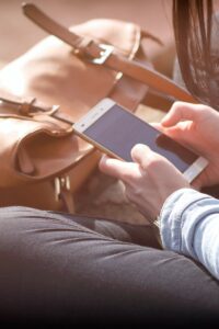 Woman sitting with smartphone and brown bag in sunlight.