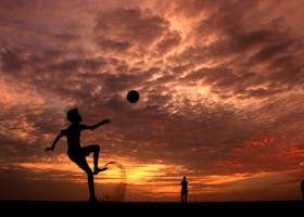 A child playing soccer on the beach at sunset in Kochi, India, creating a striking silhouette against the vibrant sky.