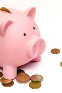 A pink piggy bank surrounded by scattered coins, symbolizing savings and financial investment.