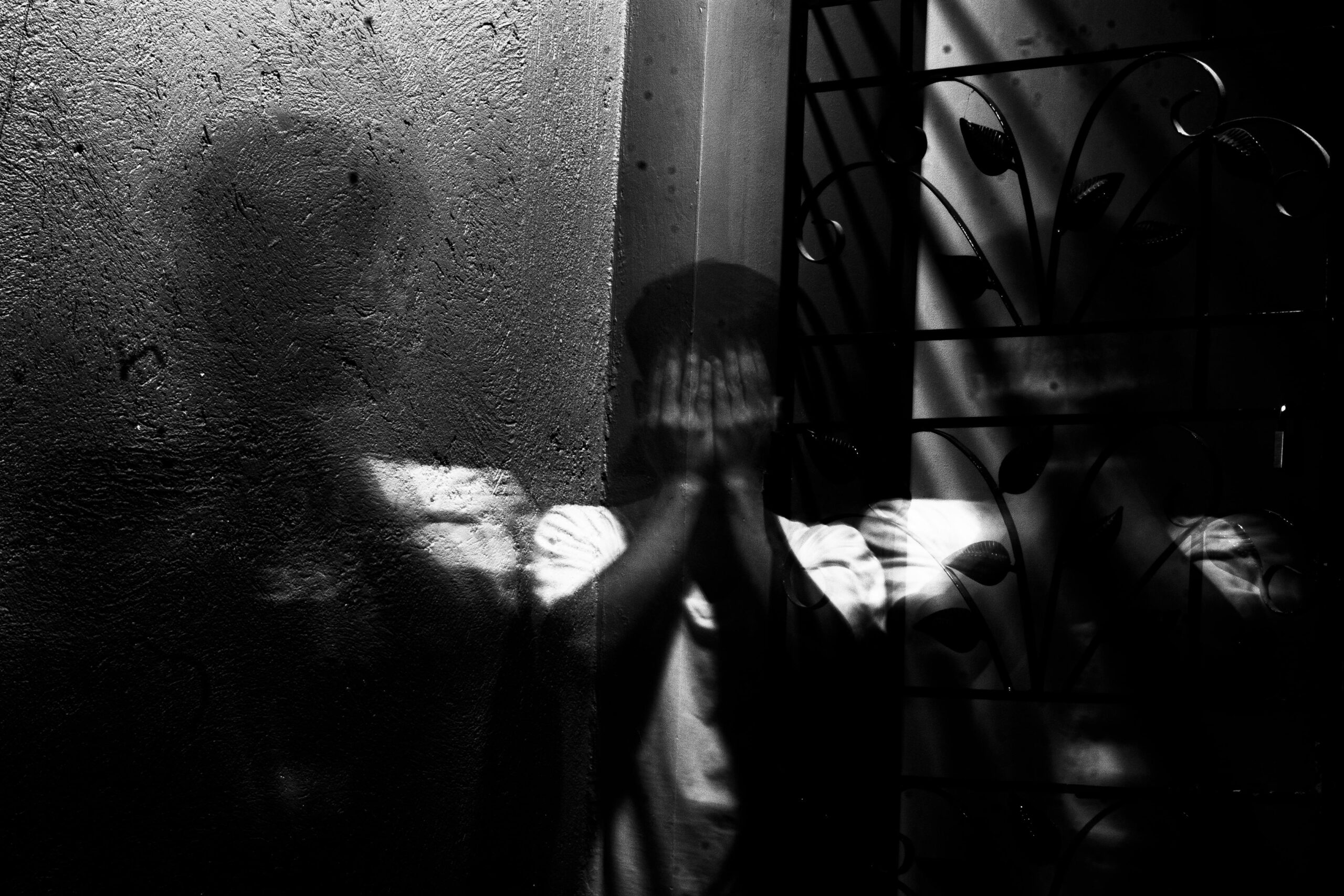 Grayscale image of a man covering his face, evoking themes of fear and introspection.